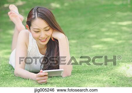 Portrait of young Japanese woman laying on grass with smartphone View Large Photo Image Stock Photograph - Portrait of young Japanese woman laying on grass with smartphone. Fotosearch