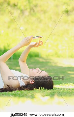 Portrait of young Japanese woman laying on grass with smartphone View Large Photo Image Stock Photography - Portrait of young Japanese woman laying on grass with smartphone. Fotosearch