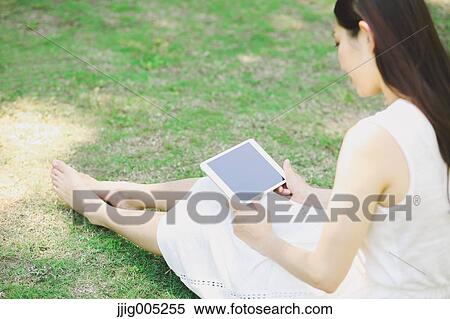 Portrait of young Japanese woman laying on grass with tablet View Large Photo Image Stock Photography - Portrait of young Japanese woman laying on grass with tablet. Fotosearch