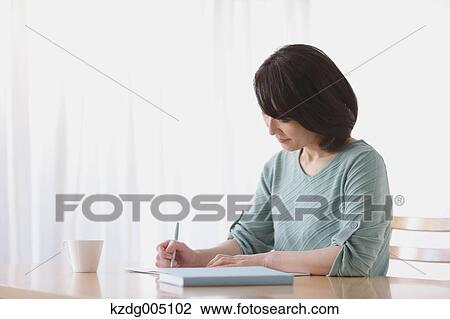 Stock Image - Senior Japanese woman doing accounting in the living room. Fotosearch