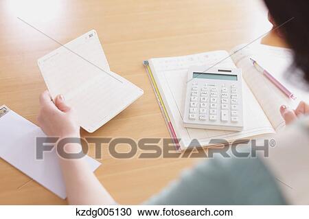 Stock Image - Senior Japanese woman doing accounting in the living room. Fotosearch