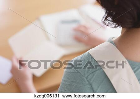 Stock Image - Senior Japanese woman doing accounting in the living room. Fotosearch