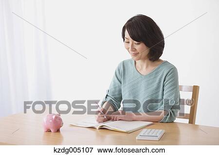 Stock Photo - Senior Japanese woman doing accounting in the living room. Fotosearch