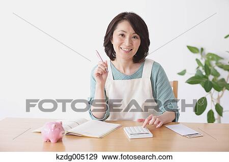 Stock Photo - Senior Japanese woman doing accounting in the living room. Fotosearch