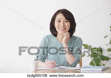 Stock Photograph - Senior Japanese woman doing accounting in the living room. Fotosearch