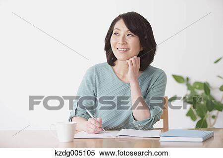 Stock Photography - Senior Japanese woman doing accounting in the living room. Fotosearch