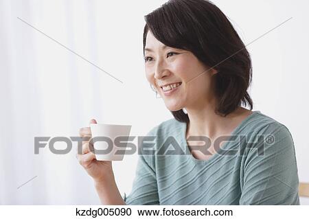 Stock Image - Senior Japanese woman having coffee in the living room. Fotosearch