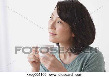 Stock Image - Senior Japanese woman having coffee in the living room. Fotosearch