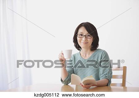 Stock Image - Senior Japanese woman having coffee in the living room. Fotosearch