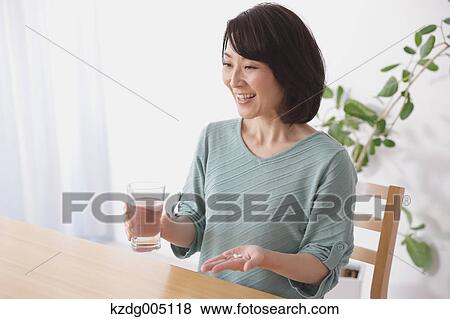 Stock Photo - Senior Japanese woman taking pills in the living room. Fotosearch