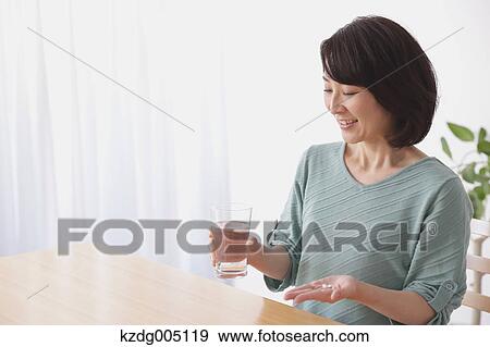 Stock Photo - Senior Japanese woman taking pills in the living room. Fotosearch