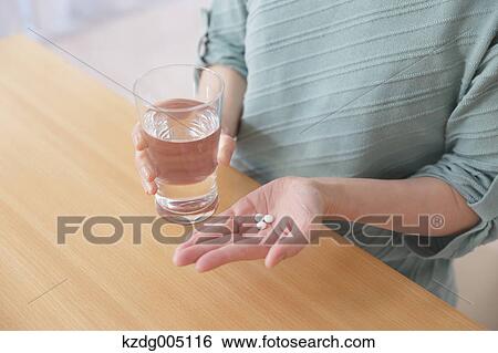 Stock Photograph - Senior Japanese woman taking pills in the living room. Fotosearch