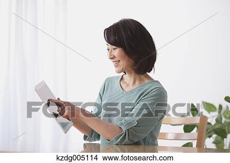 Picture - Senior Japanese woman with tablet in the living room. Fotosearch