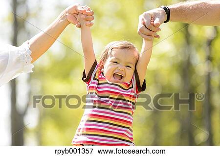 Toddler holding parents hands in a park View Large Photo Image Stock Photo - Toddler holding parents hands in a park. Fotosearch