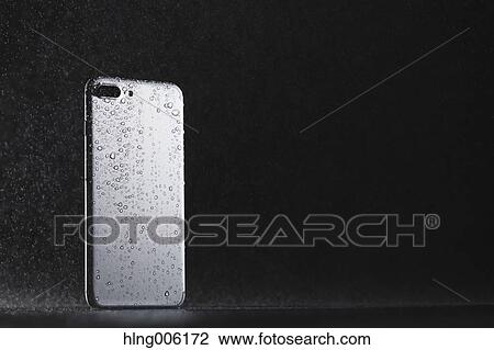 Stock Image - Waterproof smartphone covered with water. Fotosearch
