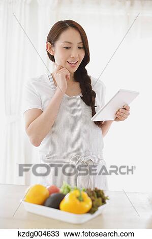 Stock Image - Young attractive Japanese woman cooking at home with tablet. Fotosearch