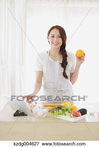 Stock Photo - Young attractive Japanese woman cooking at home with tablet. Fotosearch