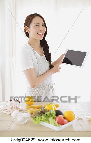 Stock Photo - Young attractive Japanese woman cooking at home with tablet. Fotosearch