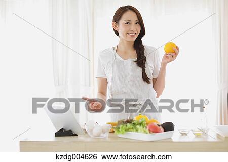 Stock Photograph - Young attractive Japanese woman cooking at home with tablet. Fotosearch