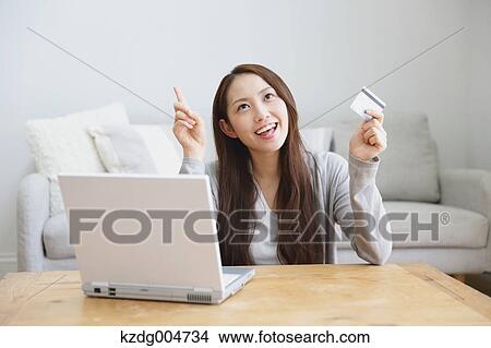 Picture - Young attractive Japanese woman doing online shopping at home. Fotosearch