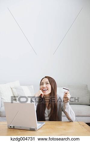 Stock Image - Young attractive Japanese woman doing online shopping at home. Fotosearch