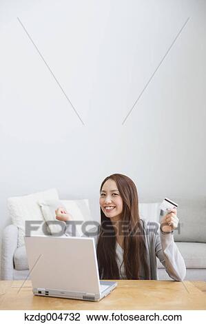 Stock Image - Young attractive Japanese woman doing online shopping at home. Fotosearch
