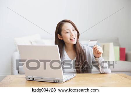 Stock Photo - Young attractive Japanese woman doing online shopping at home. Fotosearch