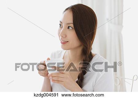 Stock Image - Young attractive Japanese woman having cofee at home. Fotosearch