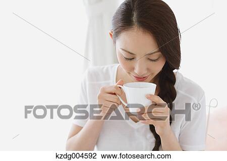 Stock Image - Young attractive Japanese woman having cofee at home. Fotosearch