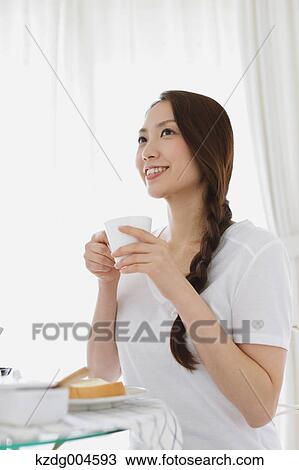 Stock Image - Young attractive Japanese woman having breakfast at home. Fotosearch
