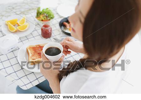 Stock Image - Young attractive Japanese woman having breakfast at home. Fotosearch