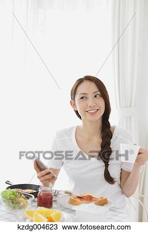 Stock Image - Young attractive Japanese woman having breakfast at home. Fotosearch