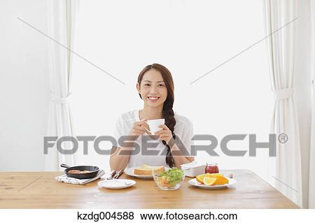 Stock Photo - Young attractive Japanese woman having breakfast at home. Fotosearch