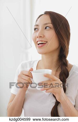 Stock Photo - Young attractive Japanese woman having cofee at home. Fotosearch