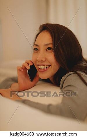 Stock Image - Young attractive Japanese woman on the phone in bed. Fotosearch