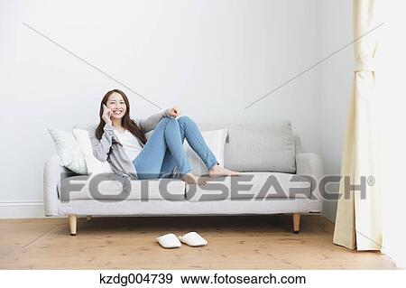 Stock Photo - Young attractive Japanese woman on the phone on the sofa. Fotosearch