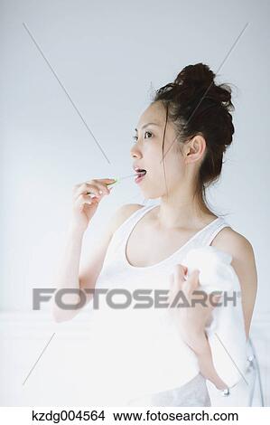 Picture - Young attractive Japanese woman brushing teeth in the bathroom. Fotosearch