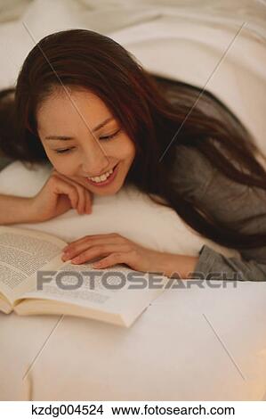 Picture - Young attractive Japanese woman reading in bed. Fotosearch