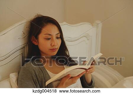 Stock Photo - Young attractive Japanese woman reading in bed. Fotosearch