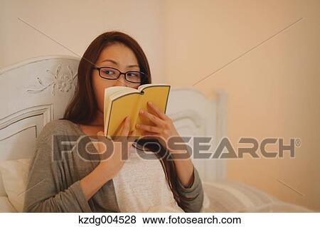 Stock Photo - Young attractive Japanese woman reading in bed. Fotosearch