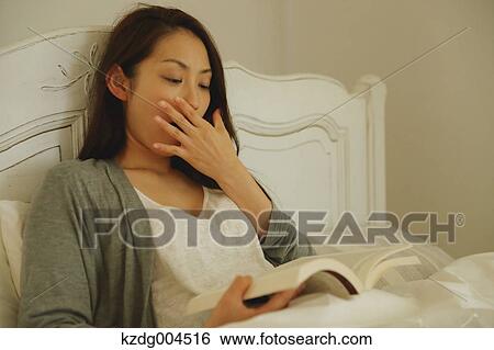 Stock Photograph - Young attractive Japanese woman reading in bed. Fotosearch