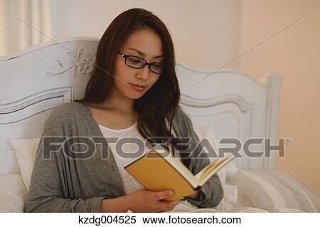 Stock Photography - Young attractive Japanese woman reading in bed. Fotosearch