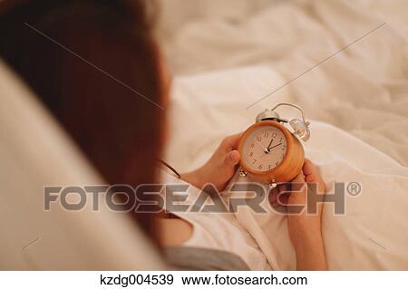 Stock Photo - Young attractive Japanese woman setting alarm clock in bed. Fotosearch