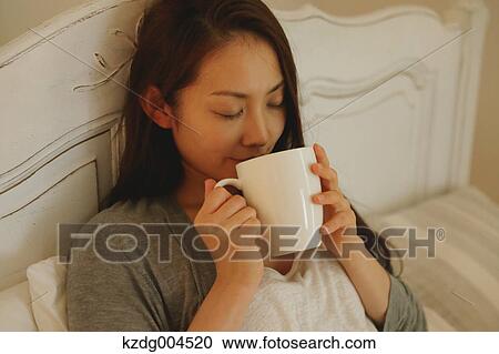 Stock Image - Young attractive Japanese woman drinking coffee in bed. Fotosearch