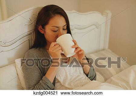 Stock Image - Young attractive Japanese woman drinking coffee in bed. Fotosearch
