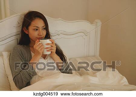 Stock Photo - Young attractive Japanese woman drinking coffee in bed. Fotosearch