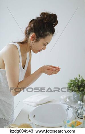 Stock Image - Young attractive Japanese woman washing face in the bathroom. Fotosearch