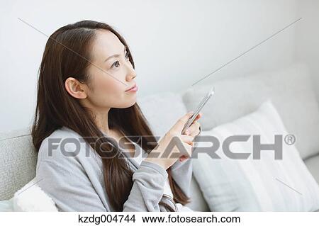 Young attractive Japanese woman with smartphone on the sofa View Large Photo Image Picture - Young attractive Japanese woman with smartphone on the sofa. Fotosearch