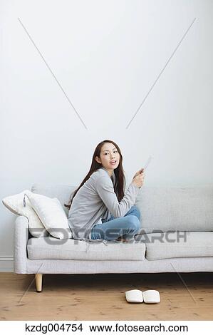 Picture - Young attractive Japanese woman with tablet on the sofa. Fotosearch