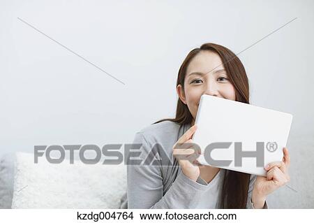Picture - Young attractive Japanese woman with tablet on the sofa. Fotosearch